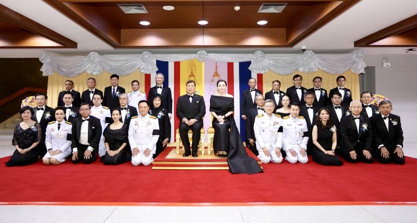 A formal portrait of dignitaries, sponsors and orchestra leadership gathered before the Thai national flag, marking the conclusion of the National Unity Concert.